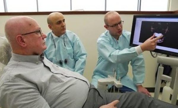 older man speaking with two dentists pointing at a screen