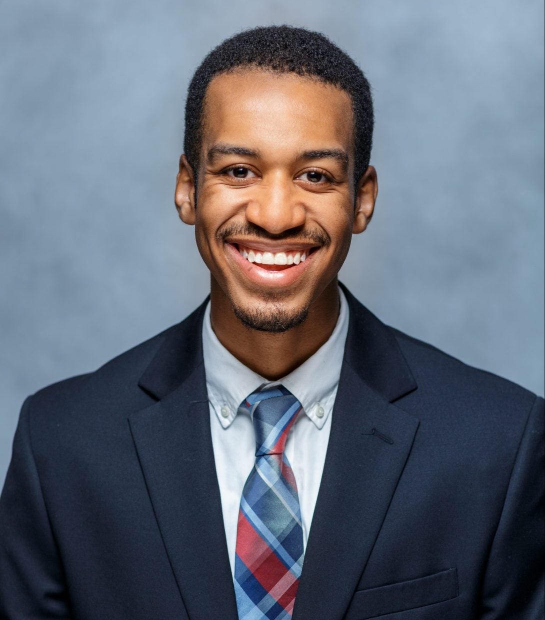 joshua williams smiling in a blue suit and wearing a blue and red tie