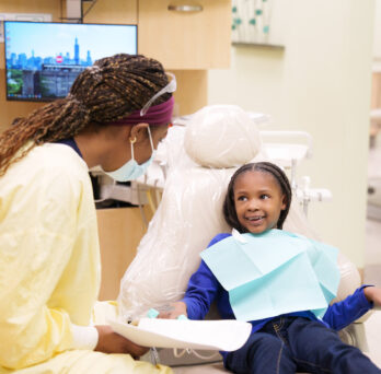 Young girl smiling at dental student in yellow scrubs 
