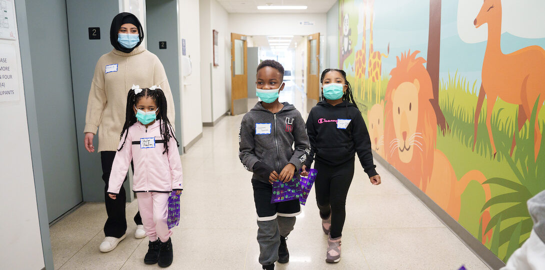A volunteer and three young students walking down the pediatric dept. hallway