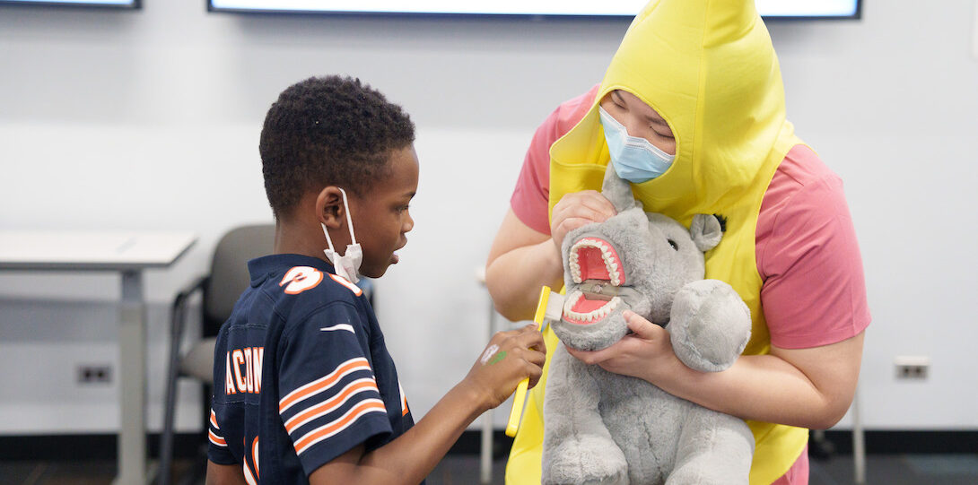 Volunteer in banana costume showing a hippo with a dental mold to a student
