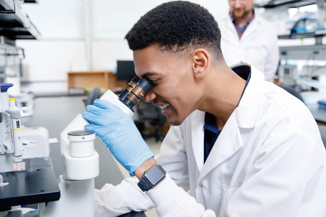 Student in a white coat looking into a microscope