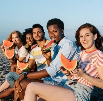 Group of people holding and eating watermelon on the beach 