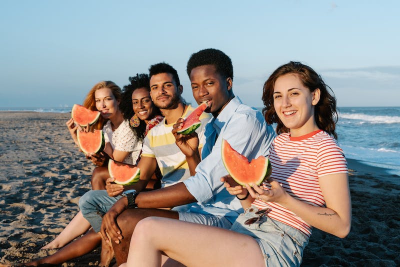 Group of people holding and eating watermelon on the beach