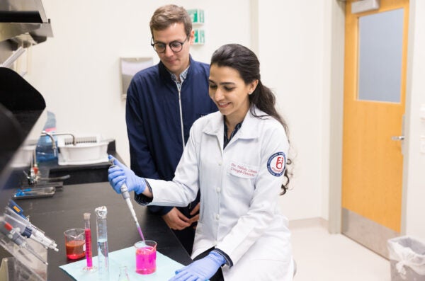 woman in lab coat using extracting pink liquid from a beaker