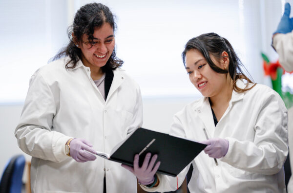 two women wearing lab coats and holding a book