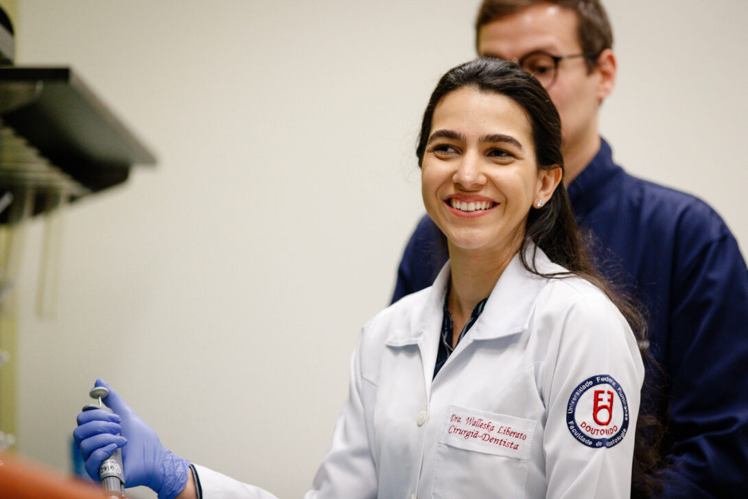 researcher in lab coat smiling while holding a syringe