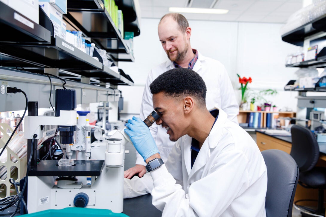 researcher and faculty wearing lab coats, researcher looking into microscope