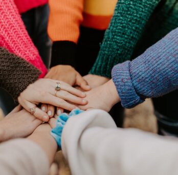 A group of women putting their hands together in a huddle
                  