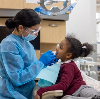 Young school girl receives oral exam in dental chair
                  