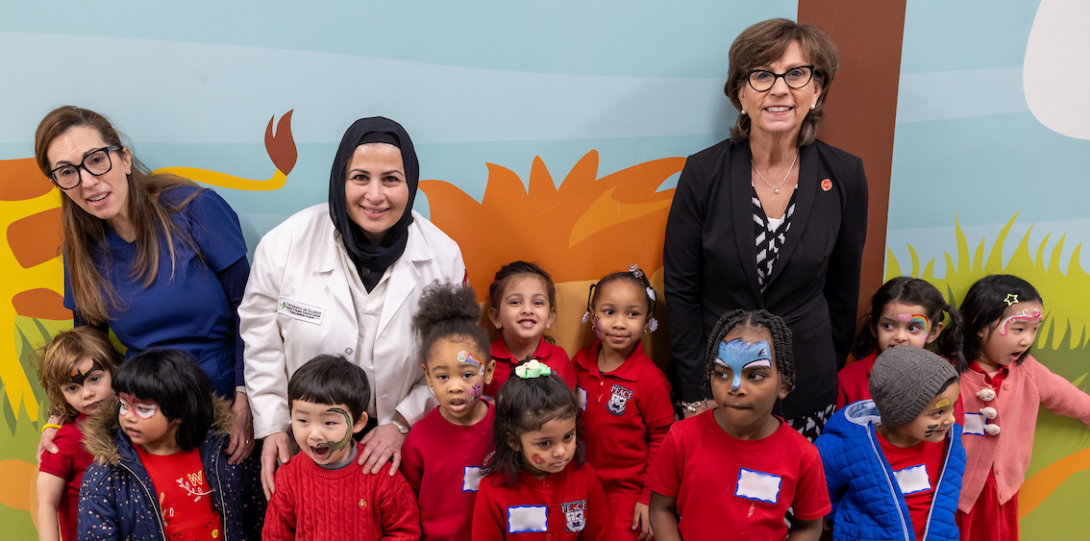 Faculty pose with school children in front of mural for Give Kids a Smile