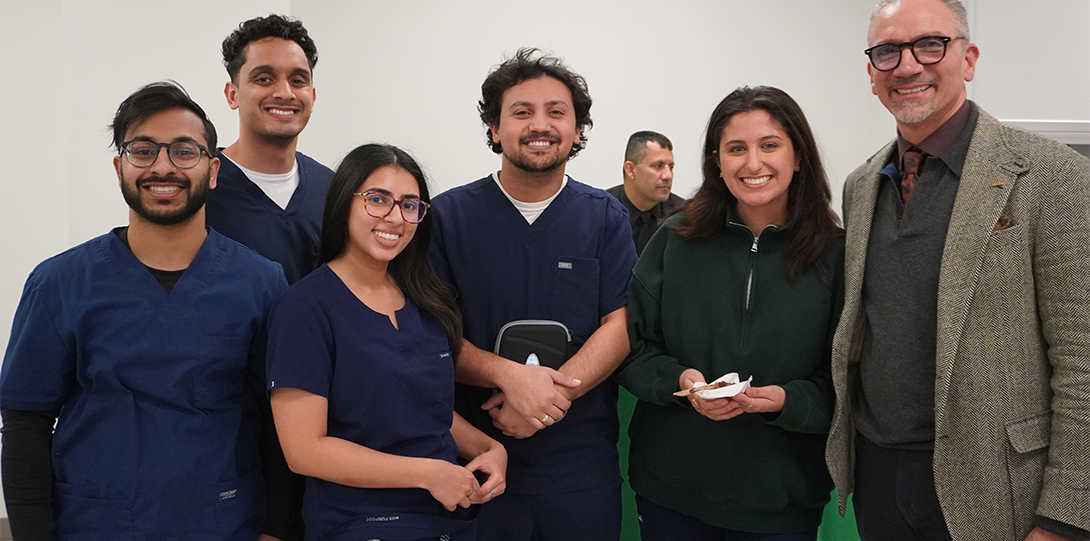 Students in blue scrubs pose with Dr. Brett Kessler