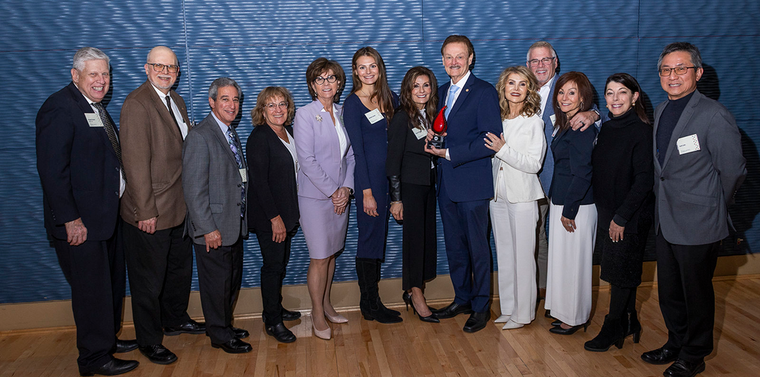 Group of 13 people posed with awardee in front of dark textured backround